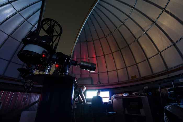Two people in an opened star dome with the telescope aimed at the sky. The people are looking at a computer screen.