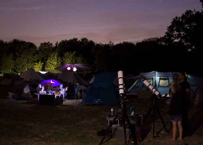 Foto van twee telescopen in het donker op een camping, omringd door tenten