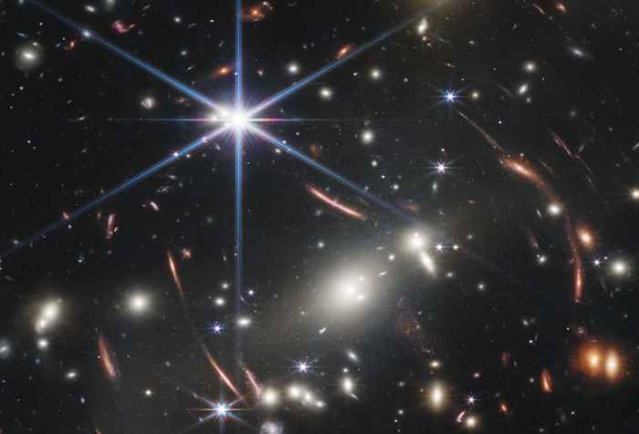 A field full of galaxies, fuzzy blobs of light with just a few stars. Some of the galaxies are deformed, a result of the bending of light by the foreground galaxies.