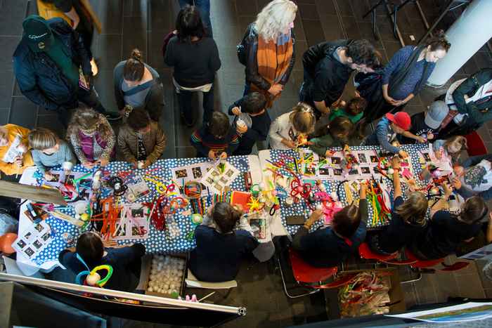 Foto van boven genomen met een tafel met kleurrijke knutselspullen omringd door kinderen en helpers.