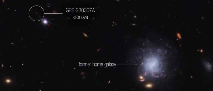 Een zwarte achtergrond met rechts onderin een cluster sterrenstelsels, vlekjes in het blauw en geel. Het grootste sterrenstelsel is blauwpaars heeft de vorm van een draaikolk. Linksbovenin staat een relatief heldere rode stip. Dit is de gammaflits die uit het grote sterrenstelsel rechtsonderin komt.