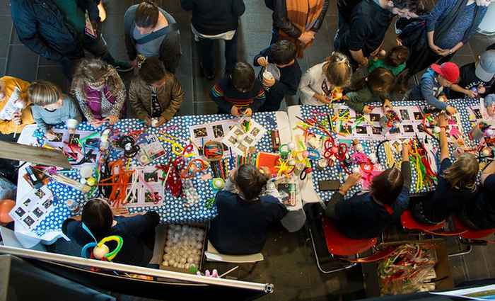 A table full of crafts materials surrounded by kids and a volunteer helping them create pulsars